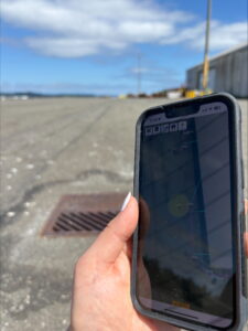 Hand holding a phone with GIS software and catch basin can be seen in the background