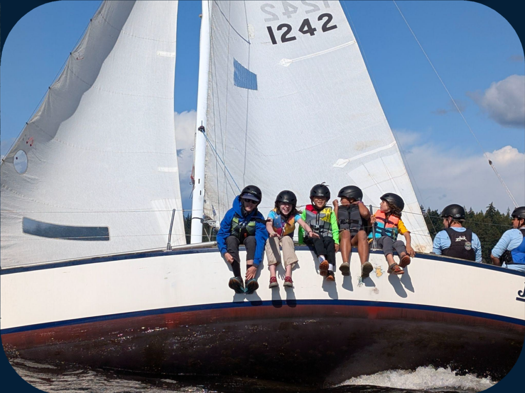 Five student sailors sitting on the side of a sailboat